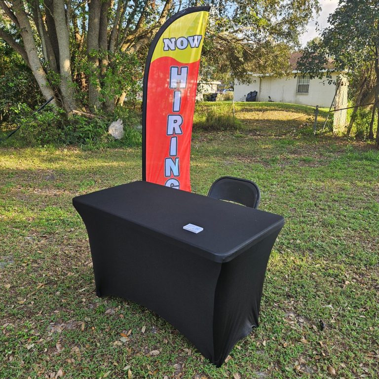 Black table with a hiring banner in a grassy outdoor setting.